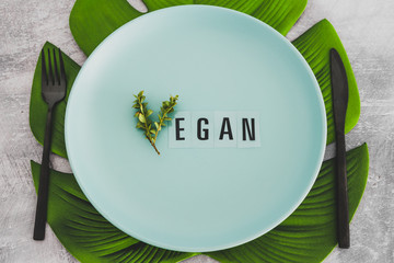 Vegan text with V made from small branches with leaves on plate with tropical leaf underneath