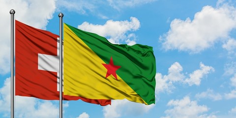 Switzerland and French Guiana flag waving in the wind against white cloudy blue sky together. Diplomacy concept, international relations.
