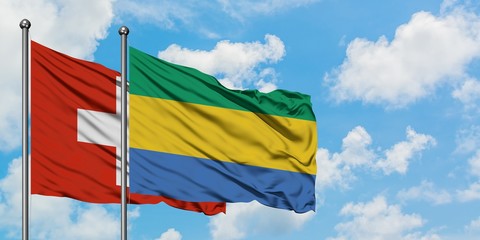 Switzerland and Gabon flag waving in the wind against white cloudy blue sky together. Diplomacy concept, international relations.