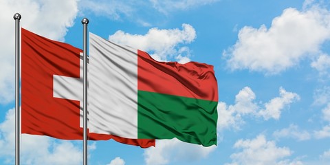 Switzerland and Madagascar flag waving in the wind against white cloudy blue sky together. Diplomacy concept, international relations.