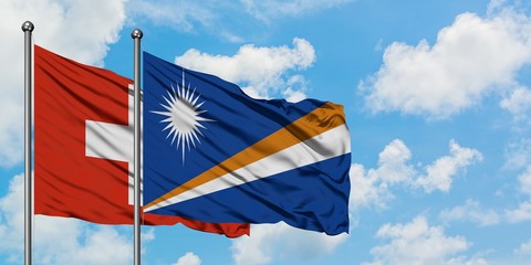 Switzerland and Marshall Islands flag waving in the wind against white cloudy blue sky together. Diplomacy concept, international relations.