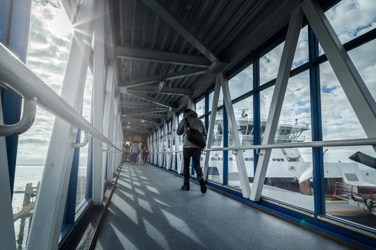 A passenger ferry terminal gangway with travellers walking with their luggage towards a ferry waiting to depart.