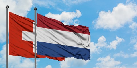 Switzerland and Netherlands flag waving in the wind against white cloudy blue sky together. Diplomacy concept, international relations.