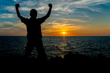 Fototapeta premium Silhouette of a man are holding arms up at the seaside and the sunset is background.