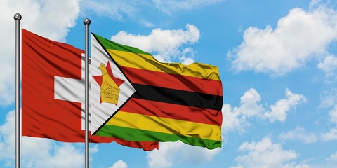 Switzerland and Zimbabwe flag waving in the wind against white cloudy blue sky together. Diplomacy concept, international relations.