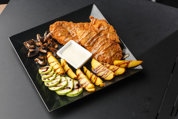 Large schnitzel with baked golden potatoes, mushrooms and zucchini on a black background. Top view....