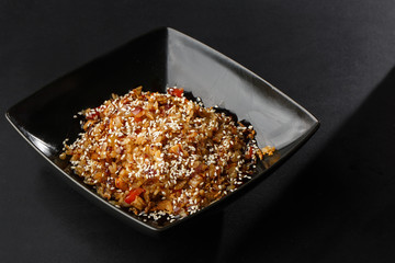Asian fried rice with eggs, tomatoes, chilli and sesame close-up on a plate, horizontal view from above. Nigerian food party: Jollof rice with fried onion close-up on a plate.
