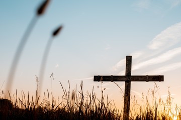 Low angle shot of a handmade wooden cross in a grassy field with a beautiful sky in the background
