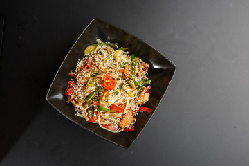 Chicken noodles bowl with vegetable. Udon stir-fry noodles with chicken meat and sesame in bowl on dark stone background copy space. Spaghetti pasta with chicken and vegetable. Horizontal photo.