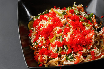 Caviar noodles bowl with vegetable. Udon stir-fry noodles with chicken meat and sesame in bowl on dark stone background copy space. Spaghetti pasta with chicken and vegetable. Horizontal photo.