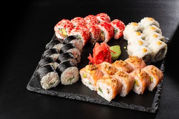 Various kinds of sushi served on black background. Sushi menu for Japanese food. Japanese sushi set. Rolls with tuna, salmon, shrimp, crab, caviar and avocado. Horizontal photo.