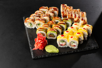 Various kinds of sushi served on black background. Sushi menu for Japanese food. Japanese sushi set. Rolls with eel, shrimp, crab, caviar, american cheese and avocado. Horizontal photo.