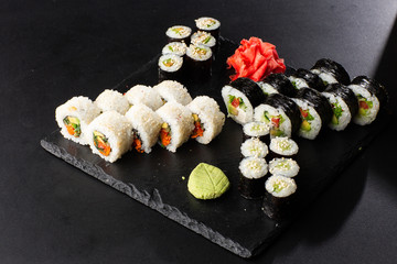 Various kinds of sushi served on black background. Sushi menu for Japanese food. Japanese sushi set. Vegan rolls and maki with carrot, cucumber, tomato and avocado. Horizontal photo