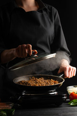 Chef cooks, fries in a pan. Cooking. Smoke and steam under the lid. Vertical shot.
