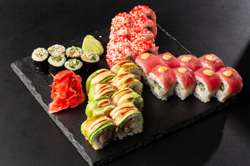 Various kinds of sushi served on black background. Sushi menu for Japanese food. Japanese sushi set. Rolls and maki with tuna, salmon, shrimp, crab, caviar and avocado. Horizontal photo.