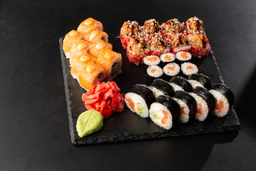 Various kinds of sushi served on black background. Sushi menu for Japanese food. Japanese sushi set. Rolls with tuna, salmon, shrimp, crab and avocado. Horizontal photo.