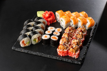 Various kinds of sushi served on black background. Sushi menu for Japanese food. Japanese sushi set. Rolls with tuna, salmon, shrimp, crab and avocado. Horizontal photo.