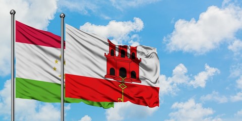 Tajikistan and Gibraltar flag waving in the wind against white cloudy blue sky together. Diplomacy concept, international relations.