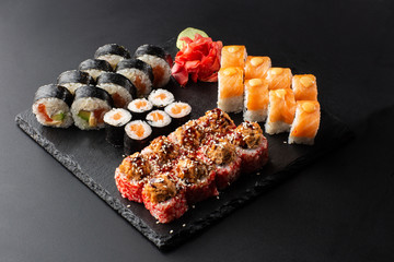 Various kinds of sushi served on black background. Sushi menu for Japanese food. Japanese sushi set. Rolls with tuna, salmon, shrimp, crab and avocado. Horizontal photo.