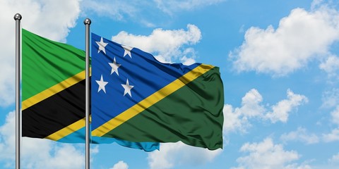 Tanzania and Solomon Islands flag waving in the wind against white cloudy blue sky together....