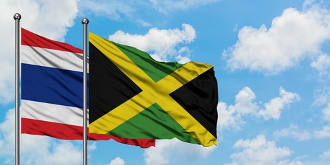 Thailand and Jamaica flag waving in the wind against white cloudy blue sky together. Diplomacy concept, international relations.