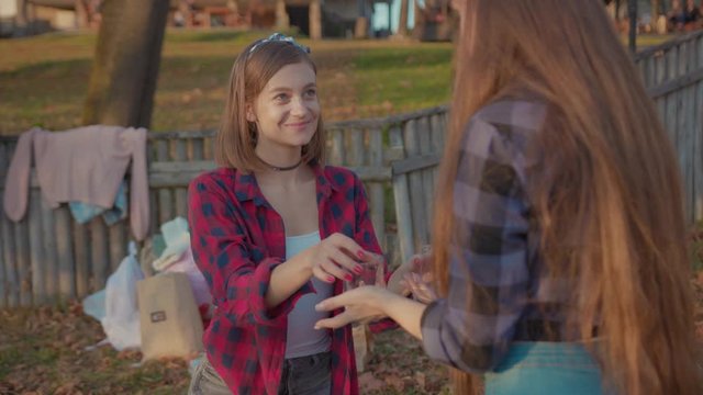 Beautiful young woman on date giving glasses to a girlfriend tasting drinks on picnic. Pretty romantic girls enjoying weekend time together. Love and romance concept.