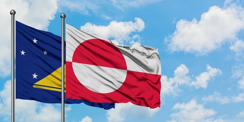 Tokelau and Greenland flag waving in the wind against white cloudy blue sky together. Diplomacy concept, international relations.