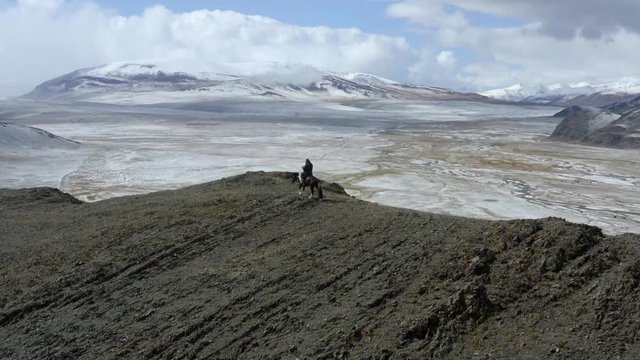 Aerial, orbit, drone shot, of a man riding a horse, on the top of a mountain ridge, on a sunny day, in the Altai mountains, near Bayan-Olgii, in Mongolia