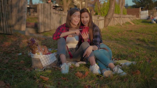 Attractive young fashion women sitting together on grass using smartphone laughing fun content dating in nature in the countryside.