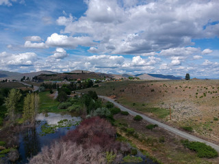Fototapeta na wymiar Tremendous aerial photography of picturesque Alta Lake State Park with an amazing and bright blue sky cumulus clouds reflecting in the water with a semi desert terrain and mountains in washington