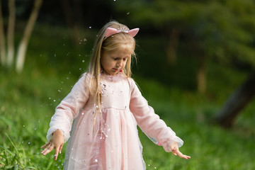 Stylish little girl with blonde hair throwing confetti in the park. Birthday celebration outdoor, fun kid leisure