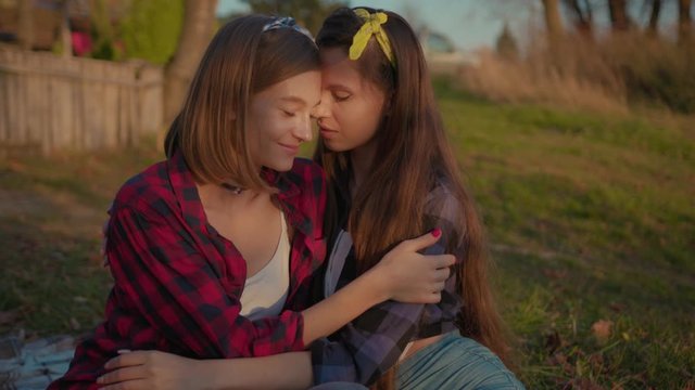 Charming young women kissing gently loving each other stroking touching face skin enjoying romantic tender moments on picnic date in the countryside.