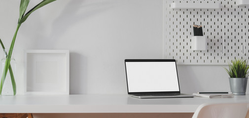 Minimal workspace with open blank screen laptop computer and mock up frame with decorations