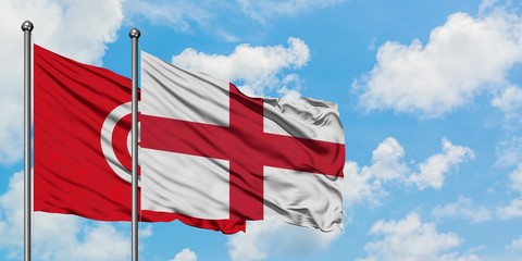 Tunisia and England flag waving in the wind against white cloudy blue sky together. Diplomacy concept, international relations.