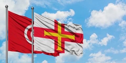 Tunisia and Guernsey flag waving in the wind against white cloudy blue sky together. Diplomacy concept, international relations.