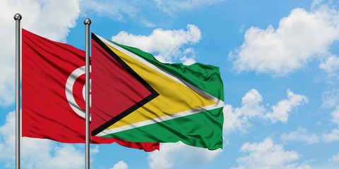 Tunisia and Guyana flag waving in the wind against white cloudy blue sky together. Diplomacy concept, international relations.