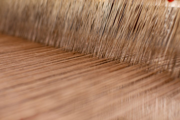 Fototapeta premium Close-up weaving cotton on manual loom. Selective focus of cotton thread on weaver machine. Abstract background cotton thread handmade. to design element background banner and artwork