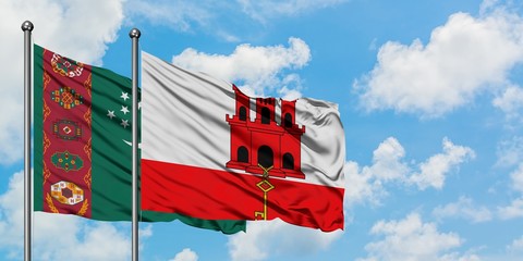Turkmenistan and Gibraltar flag waving in the wind against white cloudy blue sky together....