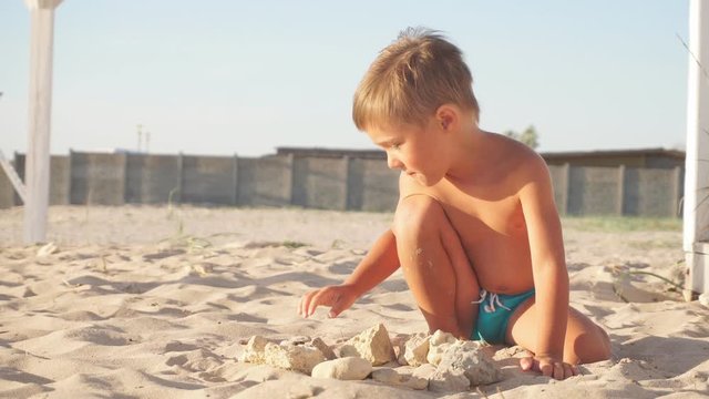 small boy plays at the windy seaside with stones.
