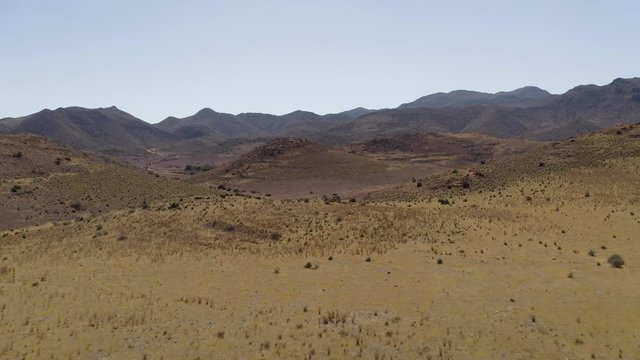 Aerial Drone footage of dry empty spanish desert with vegetation and mountains in Andalusia, Tabernas desert afternoon. Blue sky, Almeria, spain, western, far west, Sierra Nevada. 4K UHD.