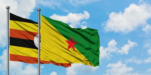 Uganda and French Guiana flag waving in the wind against white cloudy blue sky together. Diplomacy concept, international relations.
