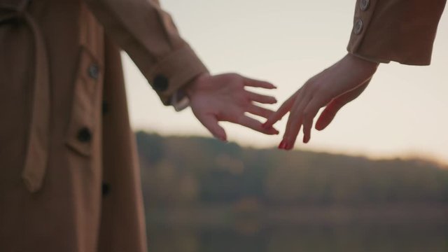 Beautiful hands of women couple holding tight parting on outdoor background. Close-up lesbian girls parting hands staying at lake under sunset sky. Love and relationship concept.
