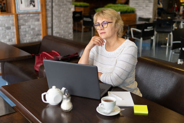 A woman with a laptop works in a cafe, she watches social networks.