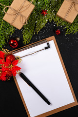 Christmas composition. Girlanda with Christmas ornaments and gifts on black background and blank notepad. Christmas, winter, new year concept. Flat lay, top view, copy space. © Julio Ricco