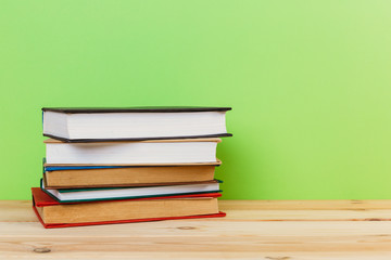 Simple composition of many hardback books, raw of books on wooden table and light green background