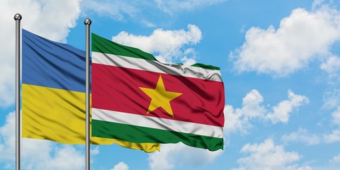 Ukraine and Suriname flag waving in the wind against white cloudy blue sky together. Diplomacy concept, international relations.