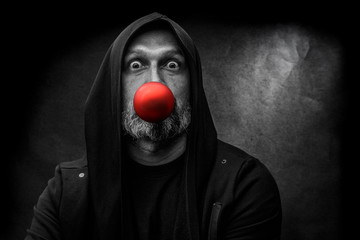 Black and white portrait of a bald bearded man in a hood with red christmas ball on a dirty gray background. Young Santa concept.