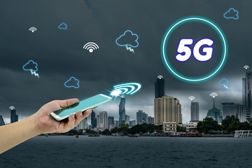 hand holding mobile smart phone with cityscape,5G network interface and icon concept