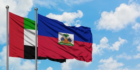United Arab Emirates and Haiti flag waving in the wind against white cloudy blue sky together....