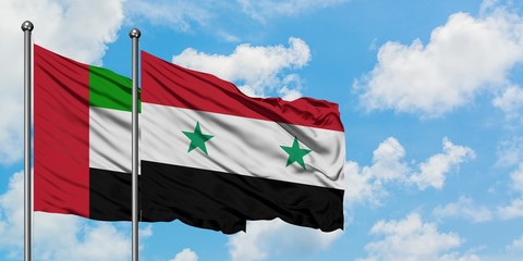 United Arab Emirates and Syria flag waving in the wind against white cloudy blue sky together....